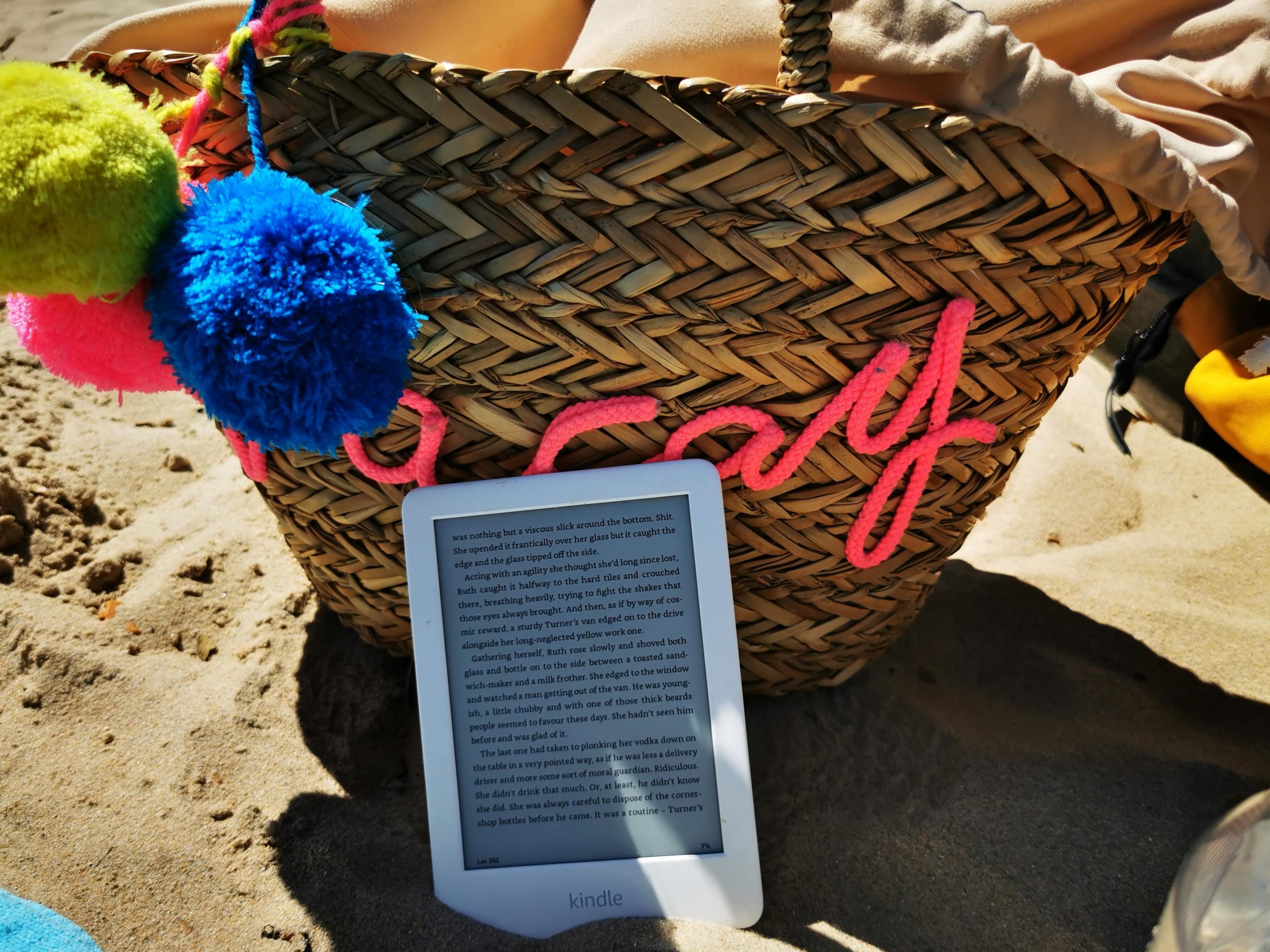 reading - kindle lent against beach bag on the sand